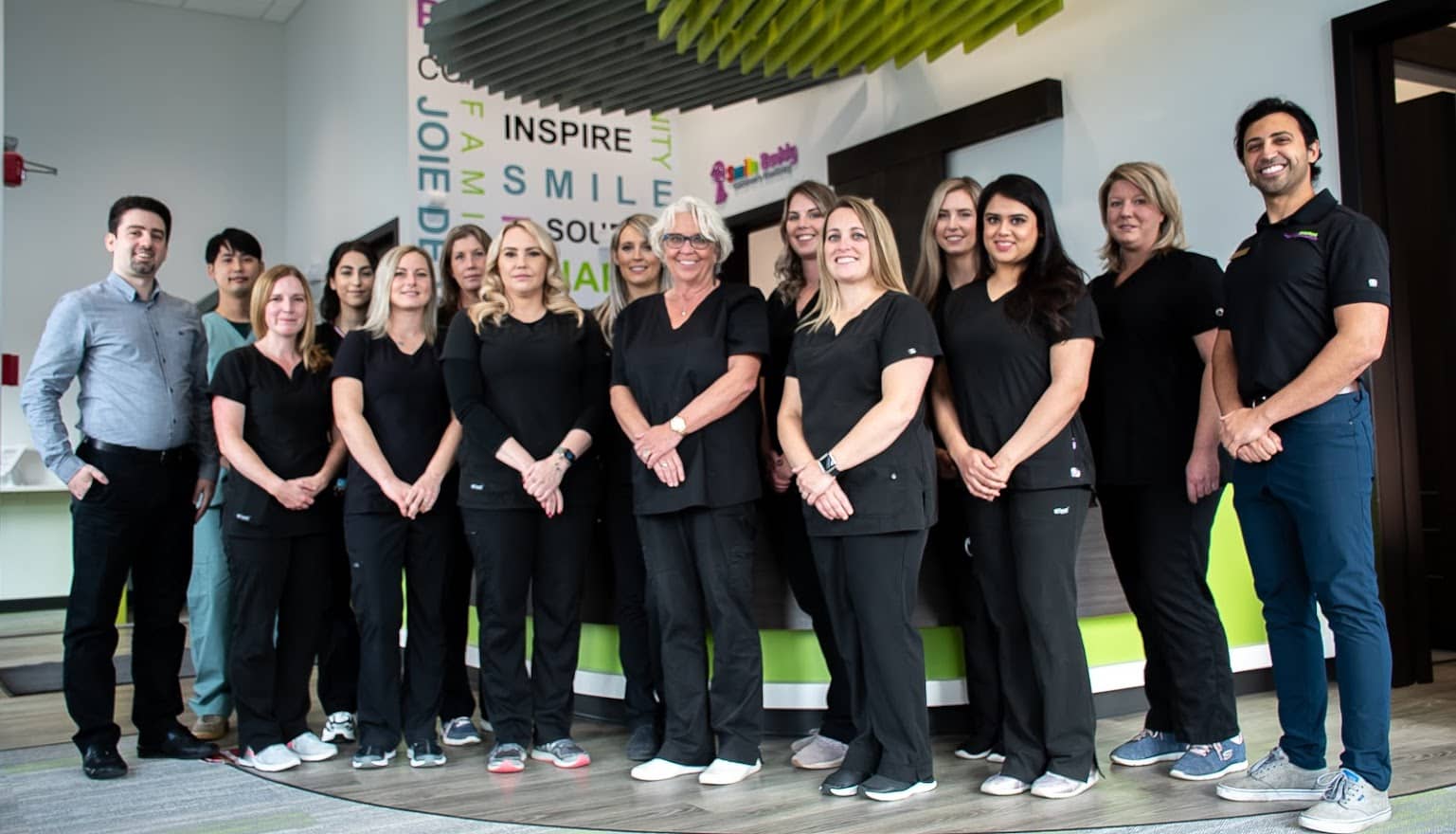 Group photo of 15 Hometown Orthodontics team members, posing together with smiles in front of a clinic backdrop